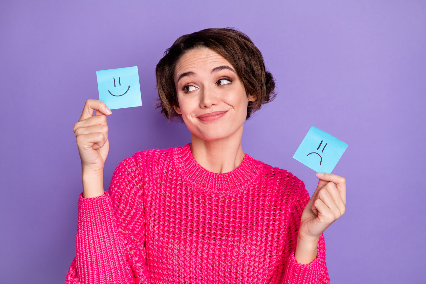 Woman in a pink sweater deciding between a smiley-face and a frowny-face sticky note