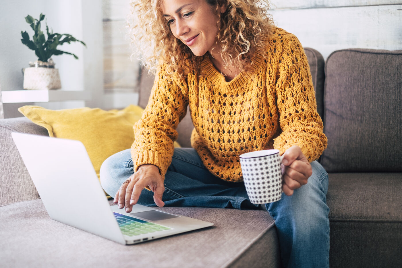 Smiling woman in a yellow sweater working on her laptop with a cup of coffee