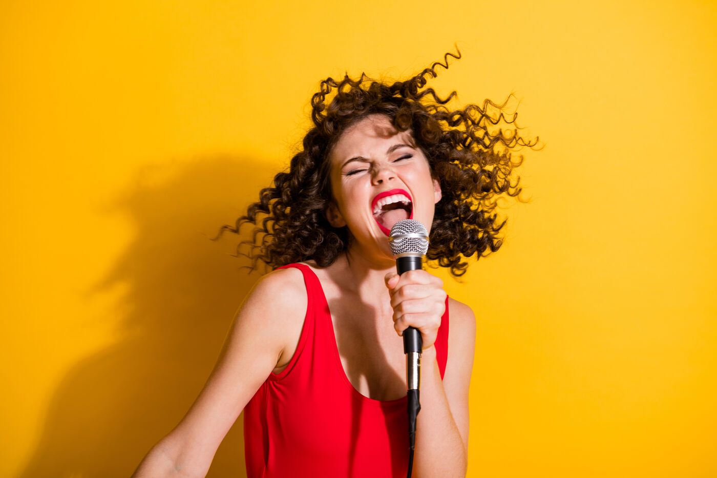 Joyful woman singing into a microphone against a bright yellow wall